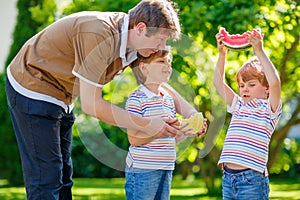 Two little preschool kid boys and father eating watermelon