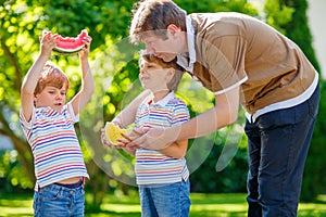 Two little preschool kid boys and father eating watermelon