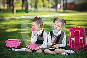 Two Little school girls with pink backpack sitting on grass after lessons and thinking ideas, read book and study