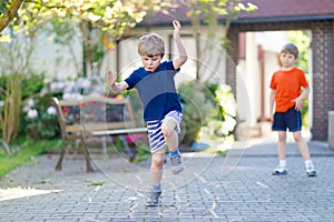 Two little school and preschool kids boys playing hopscotch on playground