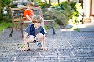 Two little school and preschool kids boys playing hopscotch on playground