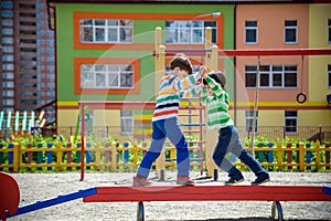 Two little school and preschool kids boys playing on playground outdoors together. children having competition standing on log