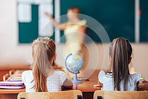 Two little schoolgirls sit at a desk in a school class and carefully listen to the teacher