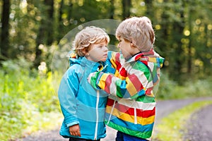 Two little sibling boys in colorful raincoats and boots walking