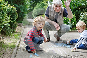 Two little sibling boys and happy grandfather painting with chalk outdoors