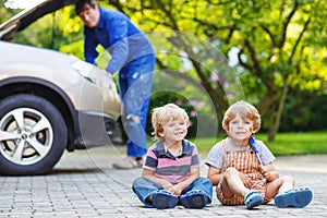 Two little sibling boys in orange safety vest during their father repairing family car