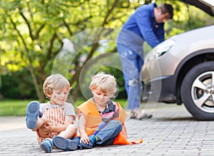 Two little sibling boys in orange safety vest during their father repairing family car