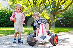 Two little sibling boys playing with pedal car in home's garden