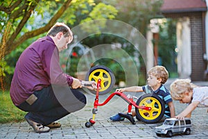 Two little sibling boys repairing bicycle wheel with father