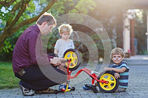 Two little sibling boys repairing bicycle wheel with father