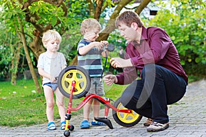 Two little sibling boys repairing bicycle wheel with father