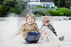 Two little sibling boys sitting on beach of river Elbe and playing together with sand