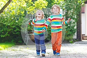 Two little sibling kid boys in colorful clothing walking hand in