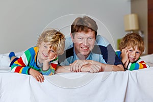 Two little sibling kid boys and dad having fun in bed after slee