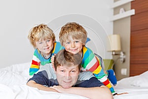 Two little sibling kid boys and dad having fun in bed after sleeping