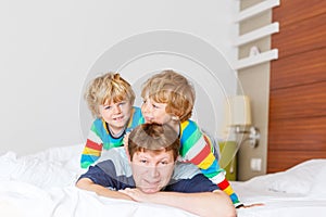Two little sibling kid boys and dad having fun in bed after sleeping