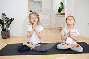 Two little siblings doing yoga at home, sitting in full lotus pose