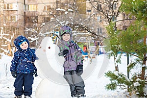 Two little siblings kids boys making a snowman, playing and having fun with snow, outdoors on cold day. Active leisure children in