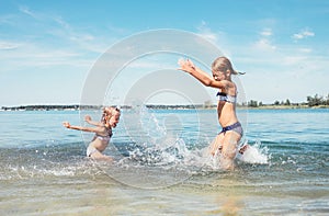 Two little sister girls fooling around in the calm sea waves splashing water to each other. Family vacation concept image photo