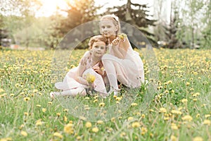 two little sisters with bouquets of dandelions sitting in a meadow.