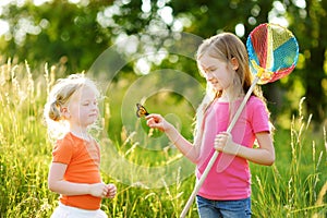 Two little sisters catching butterflies and bugs with their scoop-nets. Kids exploring nature on sunny summer day