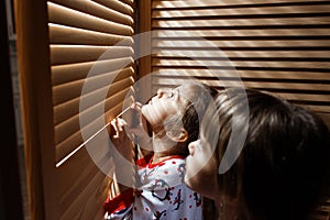 Two little sisters dressed in the pajamas are hiding in the closet with wooden doors