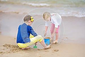 Two little sisters having fun on a sandy beach on warm and sunny summer day. Kids playing by the ocean.