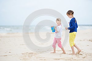 Two little sisters having fun on a sandy beach on warm and sunny summer day. Kids playing by the ocean.