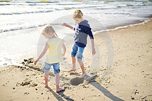 Two little sisters having fun on a sandy beach on warm and sunny summer day. Kids playing by the ocean.