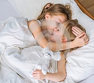 Two little sisters hugging in bed