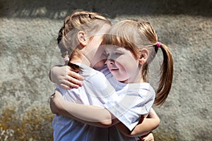 Two little sisters hugging each other smiling. Happy young kids, siblings close together, portrait. White t-shirts, care concept