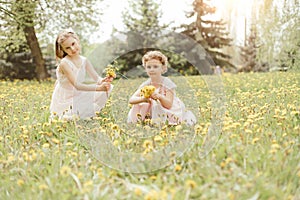 two little sisters picking dandelion flowers sitting in a meadow