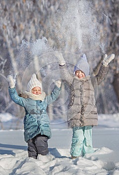 Two little sisters play and throw up a snow in winter