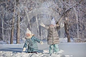 Two little sisters play and throw up a snow in winter