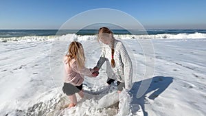 Two little sisters are playing with the waves on the beach of the Atlantic Ocean. Family time or vacation concept. 4K