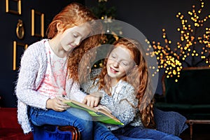 Two little sisters are reading an interesting book. The concept of Merry Christmas, New Year, family and gifts