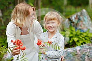 Two little sisters smiling charming girl in a forest and mountain ash in the hands of the summer