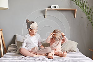 Two little sisters wearing sleep masks playing together in their bedroom, giggling and having fun, waking up in good mood,
