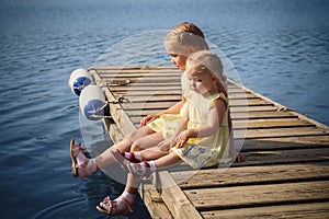 Two little sisters in yellow dresses sitting at wooden pier near