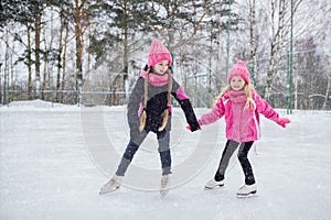 Two Little smiling girls skating on ice in pink wear.