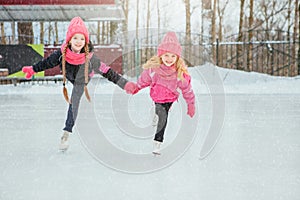 Two Little smiling girls skating on ice in pink wear and hand made scarfs. Outdoor. Winter
