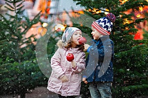 Two little smiling kids, boy and girl eating crystalized sugared apple on German Christmas market. Happy friends in