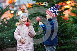 Two little smiling kids, boy and girl eating crystalized sugared apple on German Christmas market. Happy friends in