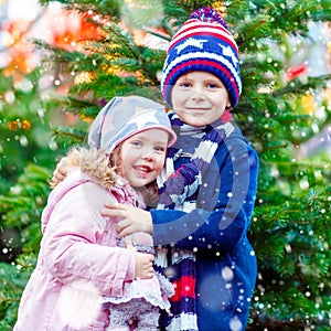 Two little smiling kids, boy and girl hugging on German Christmas market. Happy children in winter clothes with lights