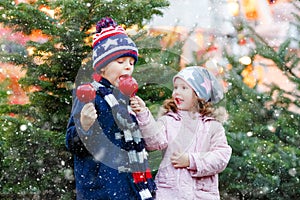 Two little smiling kids, preschool boy and girl eat sweet sugared apple on German Christmas market. Happy siblings