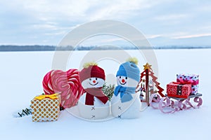 Two little snowman with the sledge, gift boxs, striped red white heart candy. Lawn covers with snow. Beautiful winter day.