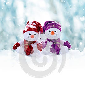 Two little snowmen the girl and the boy in caps and scarfs on snow in the winter. Background with a funny snowman