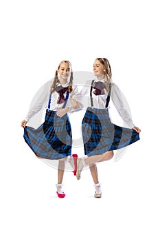 Two little stylish girls, twins in retro dresses posing isolated over white studio background. Dance mood