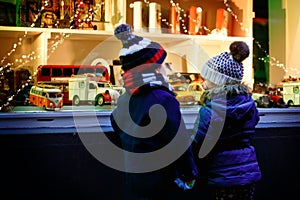 Two little toddlers, boy and girl looking on car toys in a window on Christmas time season. Fascinated children dreaming