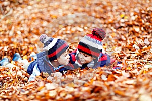 Two little twin boys lying in autumn leaves in colorful clothing. Happy siblings kids having fun in autumn forest or